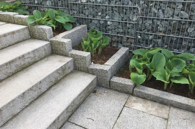 Blockstufen aus Granit neben einer Gabionenwand und bepflanzten Beeten